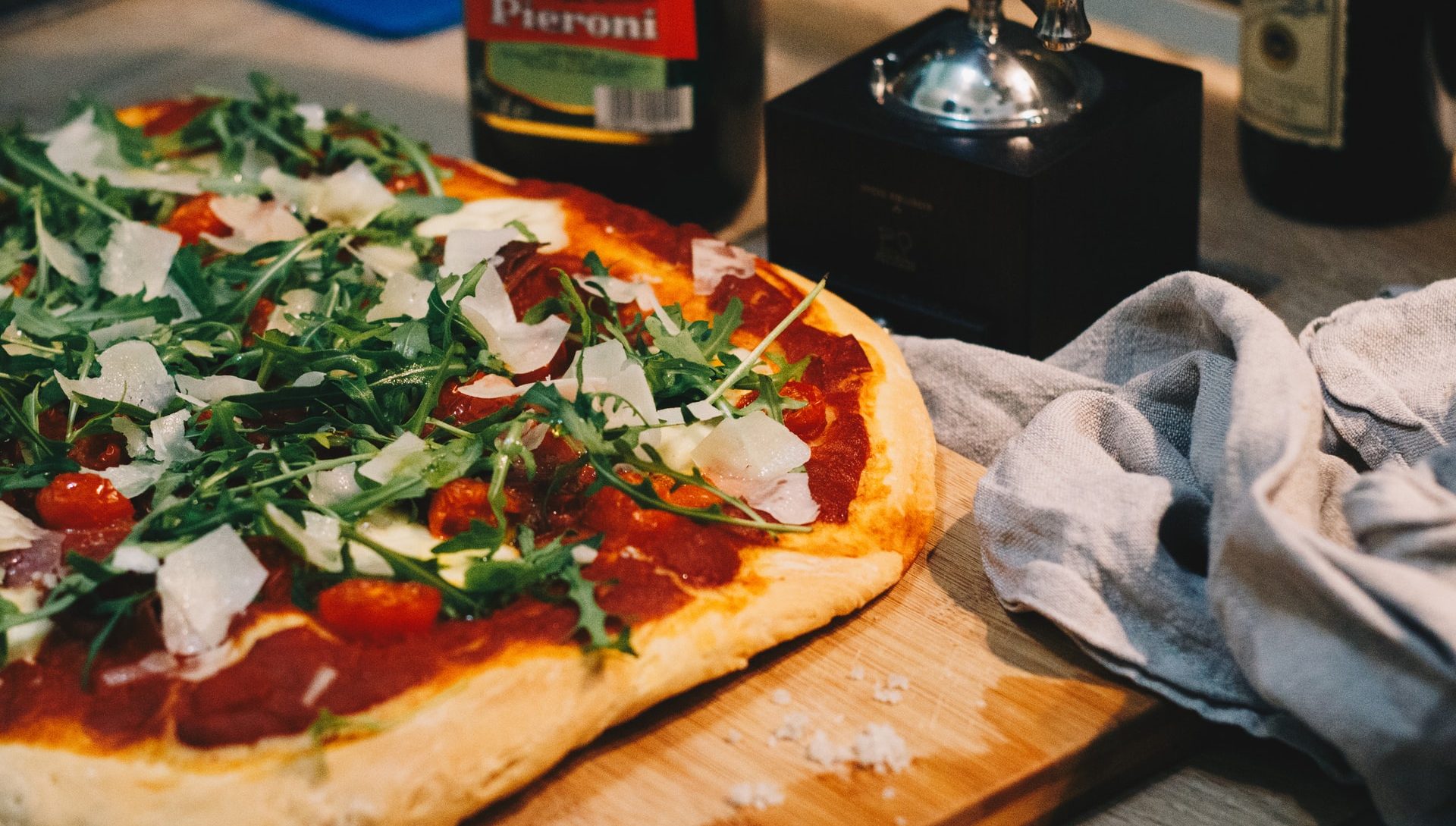 Pizza with tomatoes, greens and shaved cheese, served at the table